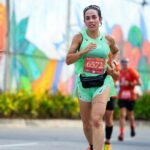 Focused female athlete running in a vibrant city marathon under sunny skies.